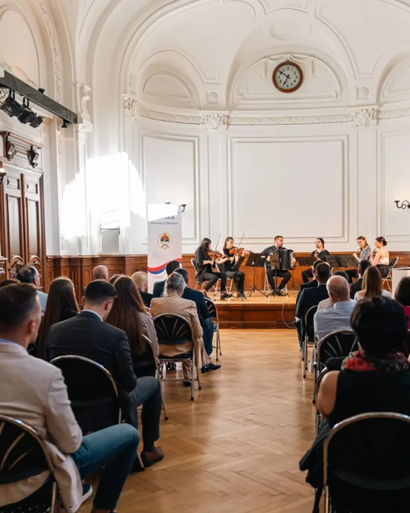 Publikum in einem Saal, auf der Bühne ein Musikensemble